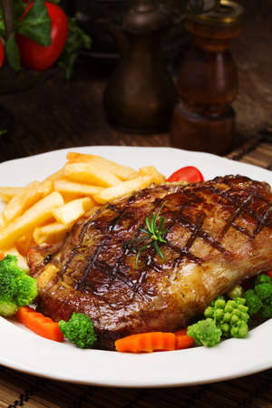 Grilled beef steak served with French fries and vegetables on a white  [FY31054696138]