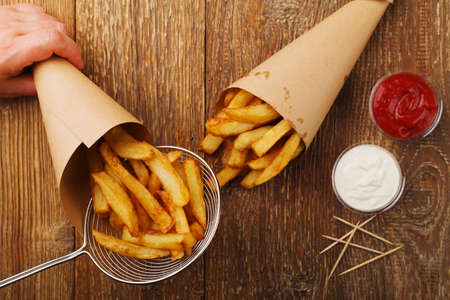 Preparation portion of Belgian fries in a paper tube, with or without a dip. On a wooden table.