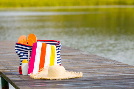 Beach bag with things to rest on the water stands on a pier over the lake.の写真素材