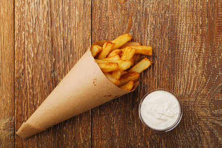 Serving Belgian fries served in a paper tube, with or without a dip. On a wooden table.の写真素材