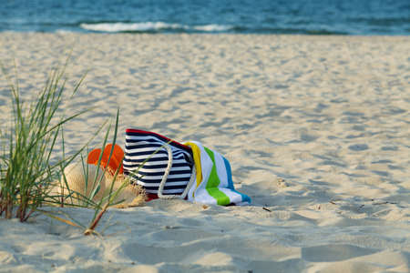Beach bag with a towel, sunglasses, thongs and hat on the beach on sea background.の写真素材