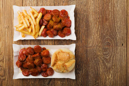 Traditional German currywurst, served with chips or bun on disposable paper tray. Wooden table as  background.の写真素材