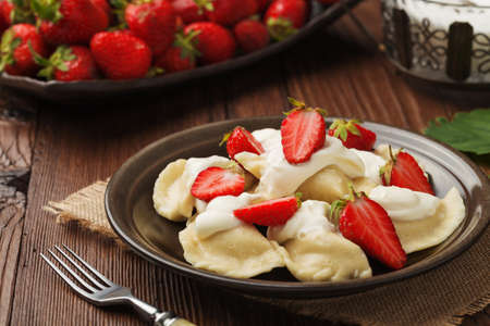 Delicious dumplings with fresh strawberries served with whipped cream and sugar. Dark wooden table as background.の写真素材