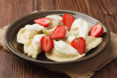 Delicious dumplings with fresh strawberries served with whipped cream and sugar. Dark wooden table as background.の写真素材
