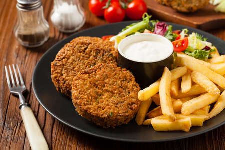 Serving of falafel and chips served on a black plate with sauce. Front view.