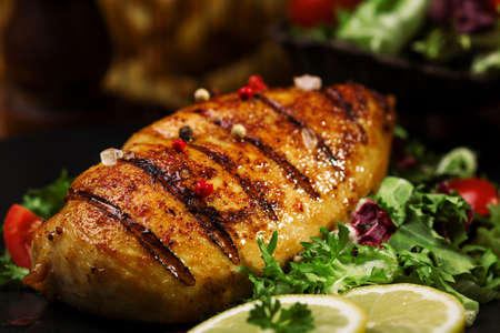 grilled chicken breast with green salad and french fries on a black plate.の写真素材