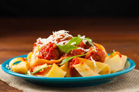 Italian pasta pappardelle with meatballs in tomato sauce, sprinkled with cheese and arugula. Front view.の写真素材