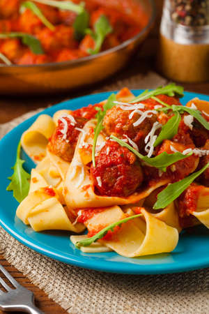 Italian pasta pappardelle with meatballs in tomato sauce, sprinkled with cheese and arugula. Front view.の写真素材