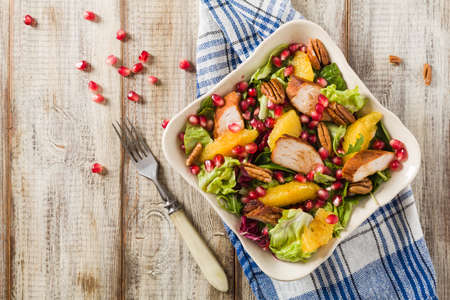 Spring salad with chicken, pomegranate, orange, pecan nuts and honey. Old table background. Top view. Wooden table background. の写真素材