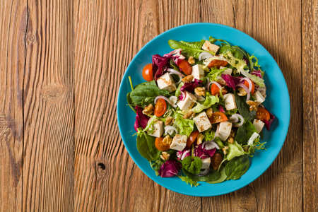 Delicious salad with tofu, tomatoes and walnuts wÅaoskimi, drizzled with a sauce of balsamic vinegar and served on a blue plate. Top view.の写真素材