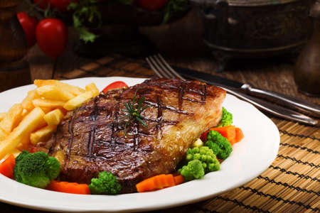 Grilled beef steak served with French fries and vegetables on a white plate.の写真素材