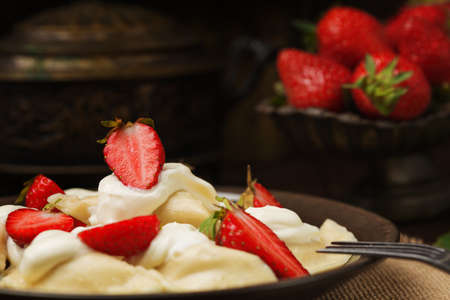 Delicious dumplings with fresh strawberries served with whipped cream and sugar. Dark wooden table as background.の写真素材