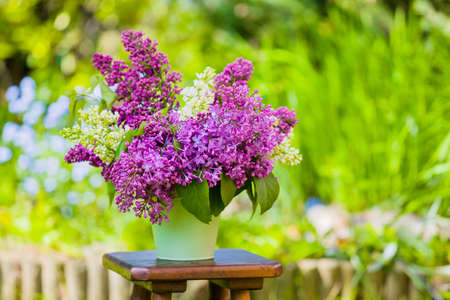 Lilac flowers in a metal vase, against the backdrop of a green garden.