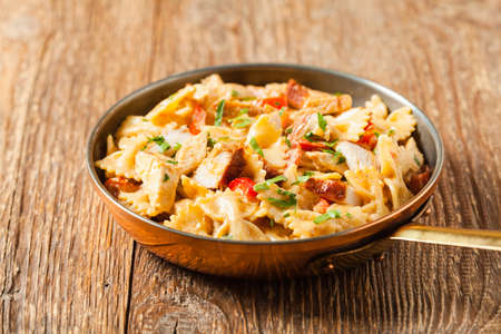 Pasta farfalle with chicken and paprika, in carbonara sauce, served in an old copper pan.  Front view.の写真素材