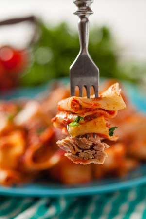 Tagliatelle pasta with tuna, in tomato sauce. Served on a blue plate, white boards in the background. Front view. Close up.の写真素材