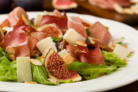 Fresh salad with figs and prosciutto with parmesan cheese and toasted almonds. Front view.の写真素材