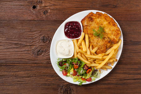 Chicken schnitzel, served with fries and salad. Natural wooden background. Top view.の写真素材