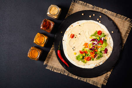 Tortilla with vegetables and hummus with chickpeas. Top view. Black background.の写真素材