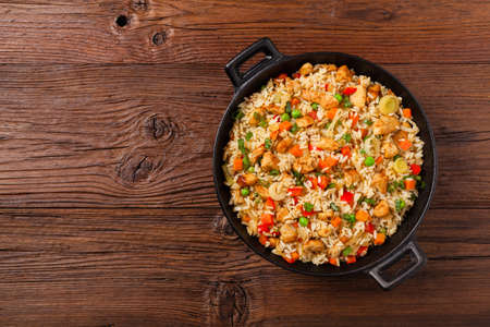 Fried rice with chicken. Prepared and served in a wok. Natural wood in the background. Top view.の写真素材
