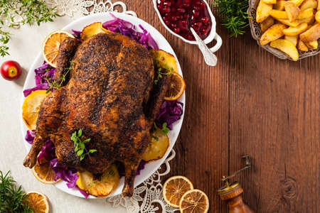 Baked whole duck, served with apples, red cabbage, oranges and roasted fritters. Natural wooden table in the background. Top view.の写真素材
