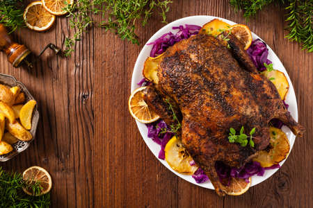Baked whole duck, served with apples, red cabbage, oranges and roasted fritters. Natural wooden table in the background. Top view.の写真素材