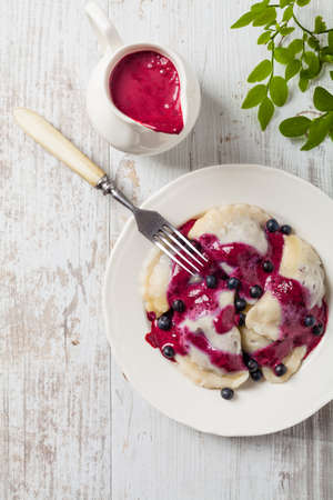 Delicious dumplings with fresh blueberries served with whipped cream and sugar or sauce. Bright, wooden background. Top view.の写真素材
