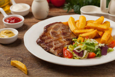 Grilled pork neck served with French fries and salad. Front view. の写真素材