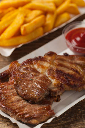 Set. Grilled pork neck served with French fries or bread and salad, served on paper trays. Front view.の写真素材