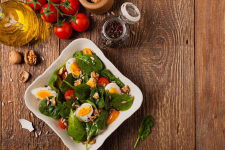 Delicious salad of fresh spinach, boiled egg, tomatoes, nuts and sunflower seeds. Top view.の写真素材