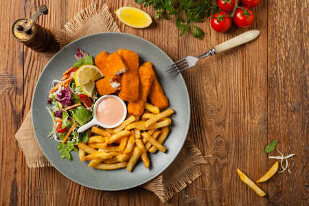 Fish sticks with fries and salad on grey plate. Top view.
