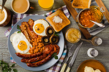 Full English breakfast, with sausage, mushrooms, beans and a fried egg. Top view.