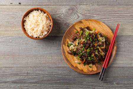 Traditional Korean Bulgogi dish.  Thinly cut, grilled beef, served with rice and vegetables. Top view. Natural wooden background.の写真素材