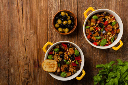 Traditional Italian caponata, served with croutons in a yellow  pot. Decorated with basil and pine nuts. Top view.の写真素材