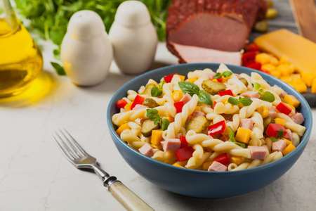 Italian fusilli pasta in a salad with ham and vegetables. Front view. Background white stoneの写真素材