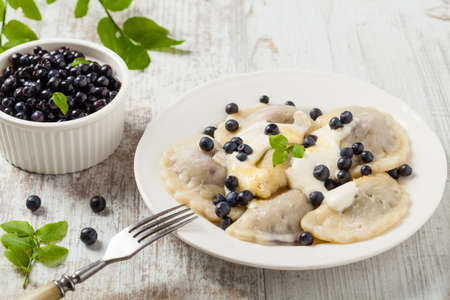 Delicious dumplings with fresh blueberries served with whipped cream and sugar or sauce. Bright, wooden background. Front view.の写真素材