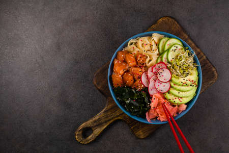 Hawaiian salmon poke bowl with seaweed, avocado, sesame seeds. Top view. Black background.