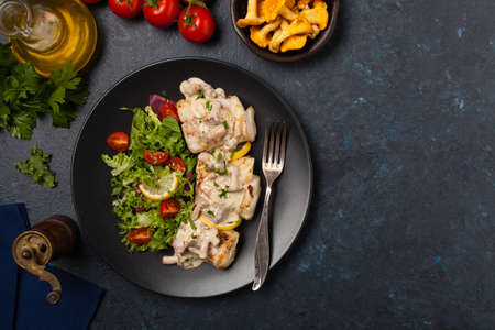 Fried cod served with mushroom sauce and salads. Portion on a black plate. Dark background.の写真素材