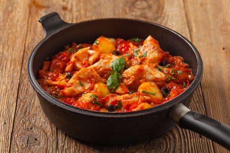 Traditionally prepared cod in Spanish. Served in tomato sauce with boiled potatoes, olive and basil. Front view.の写真素材