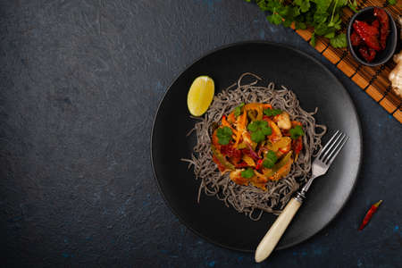 Wheat noodles with black sesame, fried in a wok with chicken and vegetables. Top view. Served on a...