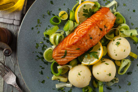 Portion of fried salmon, served with mashed potatoes and cooked leek. Top view. Gray plate, wooden background. の写真素材