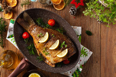 Fried carp whole. Served with lemon and cherry tomatoes. Served in a pan for frying fish.