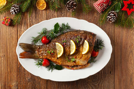 Fried carp whole. Served with lemon and cherry tomatoes on white plate. Christmas decoration. Top...