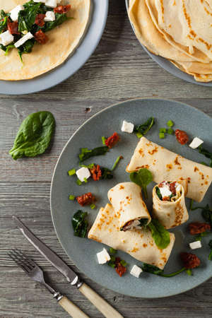 Pancakes with spinach, feta and dried tomatoes. Served on a gray plate. Wooden natural background.の写真素材