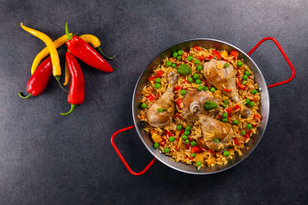 Arroz con pollo. Baked pieces of chicken with bone, rice with paprika and peas. Black background. Served on black plate or spanish pan.の写真素材