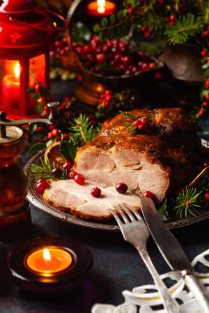 Roast pork neck in Christmas style. Dark navy blue background. Christmas accessories. Candles and lanterns in the background.の写真素材
