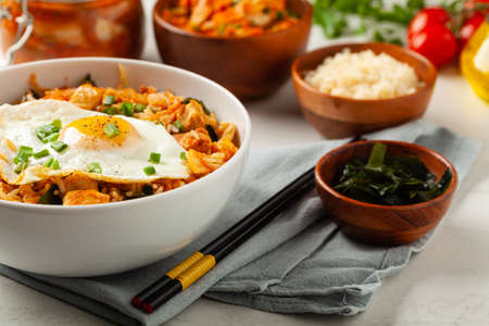 Kimchi cabbage with rice and chicken. Served in a white bowl on a light marble background. Front view.の写真素材