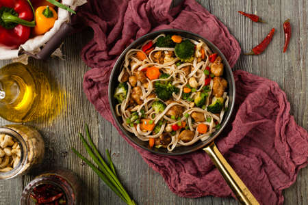 stir-fry pasta with chicken, broccoli and carrots. Top view. Gray wooden background. Served in a frying pan.の写真素材