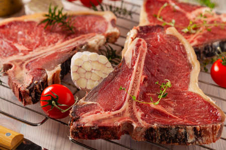 Raw t bone steak, with herbs. Grill accessories. Ready for grilling. Wooden bright background.の写真素材