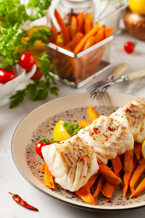 Fried pieces of cod loin, served with sweet potato fries. Light stone background.の写真素材