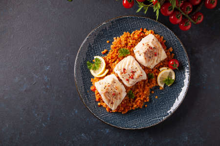 Fried pieces of cod loin, served on dark chickpeas. Dark painted background.